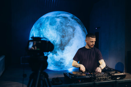 A DJ performs in a modern indoor venue featuring an illuminated moon-like sphere as the background....