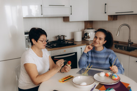 A cheerful family bonding moment of a mother and daughter painting colorful Easter eggs together in their modern kitchen.の写真素材