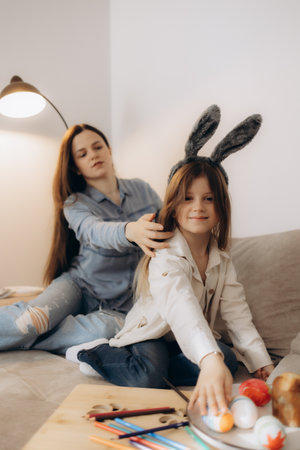 A mother lovingly interacts with her daughter during a creative indoor activity featuring colorful painted eggs, fostering a joyful and warm family connection.の写真素材