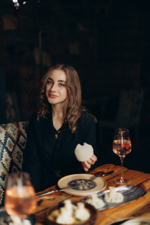A young woman smiles at a restaurant table with delicious food and a glass of wine in a cozy setting. Upscale dining experience and leisure at its finest.の写真素材