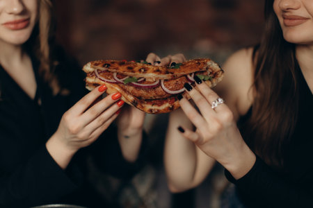 Two women sitting together sharing a deliciously grilled sandwich, enjoying quality time in a comfortable and warm setting, showcasing friendship and pleasant moments.の写真素材