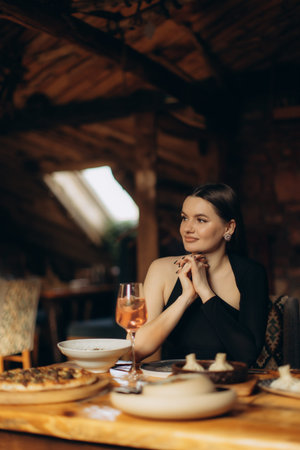 A woman sits at a wooden table in a charming rustic restaurant, enjoying a meal accompanied by a refreshing beverage. The cozy atmosphere highlights the beautiful interior design.の写真素材