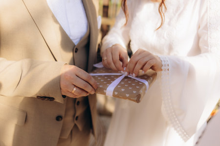 A bride and groom in formal attire together holding a beautifully wrapped gift box with heart patterns, symbolizing love and celebration during their wedding day.の写真素材