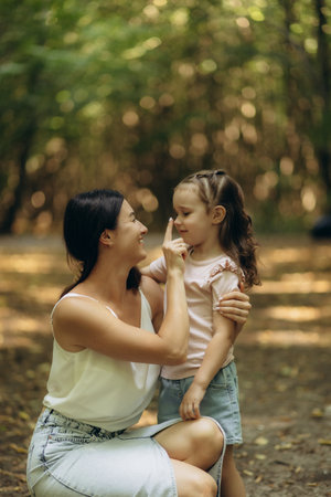 A loving mother and her young daughter share a joyful moment together in a beautiful forest, surrounded by soft sunlight and green leaves, exemplifying connection, affection, and family-oriented bonding.の写真素材
