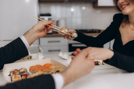 A couple shares a moment while eating sushi in a contemporary kitchen, showing connection, happiness, and culinary enjoyment. The image conveys warmth, relationships, and appreciation for food and companionship.の写真素材