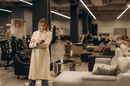 A thoughtful individual stands indoors, exploring a contemporary furniture showroom, surrounded by neatly displayed couches and chairs. The atmosphere suggests decision-making, modern decor, and technology.の写真素材