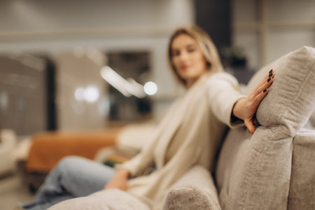 A woman dressed stylishly leans back on a comfortable sofa in a modern home interior setting. The blurred background enhances the focus on the foreground, creating a sense of relaxation and warmth.の写真素材