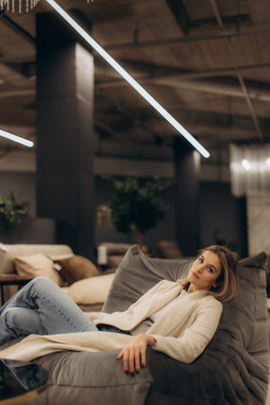 A calm woman rests on a plush sofa, set in a chic, contemporary interior environment highlighted by inviting decor and subtle lighting.の写真素材