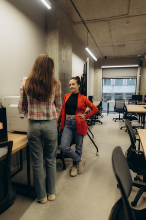 Two women stand and interact in a professional office space with an open layout design.の写真素材