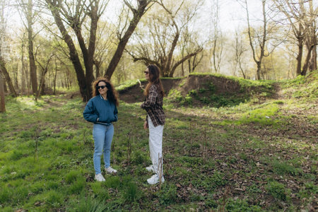 Two women stand outdoors in a tranquil forest during springtime, enjoying the fresh air and scenic surroundings while engaging in a pleasant conversation.の写真素材