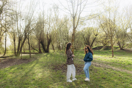 Two friends standing in a scenic park surrounded by trees, enjoying a sunny day. A natural and calming setting showcasing friendship and outdoor beauty, ideal for themes related to nature and relationships.の写真素材