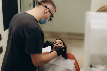 A professional dentist performing a routine dental check-up on a patient in a clinical setting. The patient appears seated in a dental chair, highlighting oral healthcare and dental procedures.の写真素材