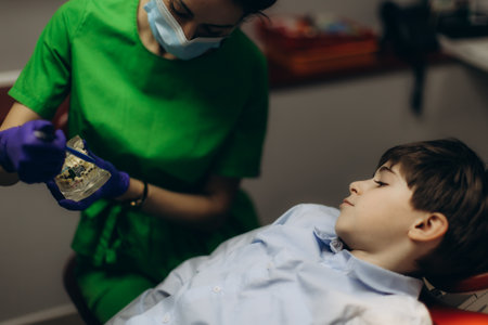 A professional dentist explaining dental procedures to a young boy with a dental model in a clinic. The scene emphasizes the importance of dental education and comfort in a clinical setting.の写真素材