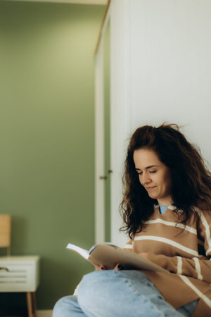 A cheerful woman enjoys an engaging book while seated in a serene room, surrounded by a calming...