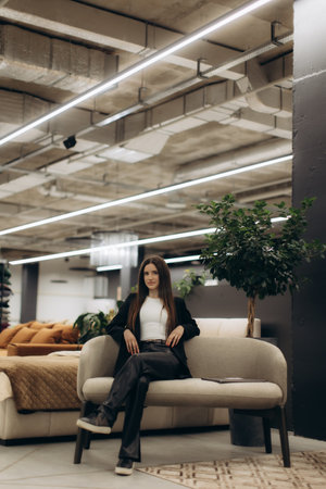 Modern interior featuring a fashionable woman seated on a sofa amidst bright lighting and decor.の写真素材