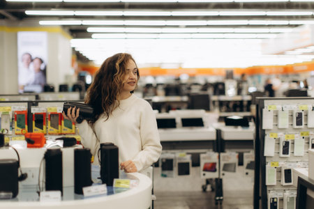 A young woman explores electronic devices in a brightly lit technology store, showcasing interest in...