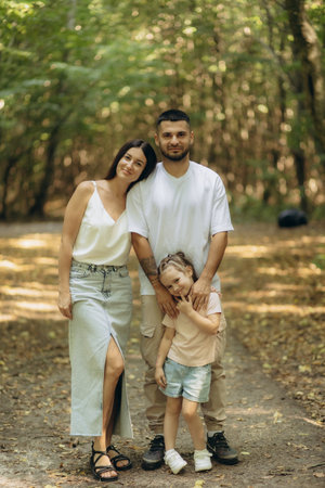A cheerful family of three enjoying a day outdoors amidst the lush greenery of a park. Capturing the joy of familial bonding, love, and connection within a natural and peaceful environment.の写真素材