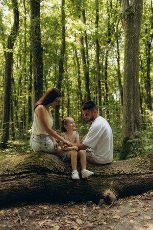 A happy family spending quality moments in a tranquil forest setting, sharing joy and bonding on a fallen tree surrounded by nature's beauty.の写真素材
