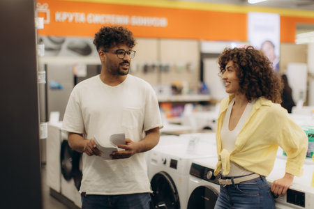 A cheerful couple exploring options for laundry appliances in a contemporary electronics showroom, discussing features and designs with interest.の写真素材