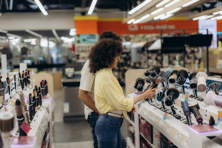 A couple explores different hair dryer models in a bright, modern electronics store. Couple buys a curling iron, hair dryer, hair straightenerの写真素材