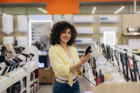 A smiling young woman examines hair care devices while shopping in a modern electronics store.の写真素材