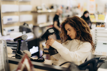 A woman browsing modern electronic appliances in a store, focusing on portable devices. Her interest reflects detailed consideration for features and quality while making a thoughtful purchase.の写真素材