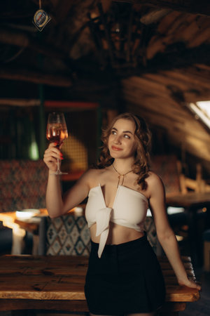 A young woman raises a glass of rosÃ© wine with a cheerful expression in a warmly lit rustic-style bar, evoking a sense of celebration and relaxation amidst an inviting wooden decor.の写真素材