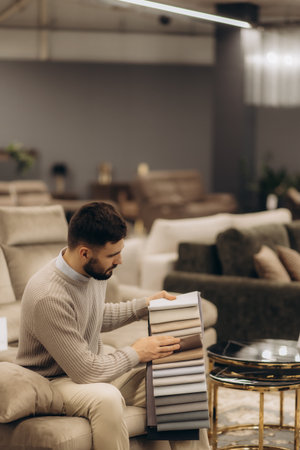 A man evaluates fabric samples while seated in a cozy modern furniture showroom. The environment emphasizes comfort and stylish decor, with neutral tones, showcasing a range of home design possibilities.の写真素材