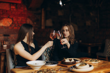 Two women enjoy a warm and delightful dining experience, clinking glasses during an elegant dinner...