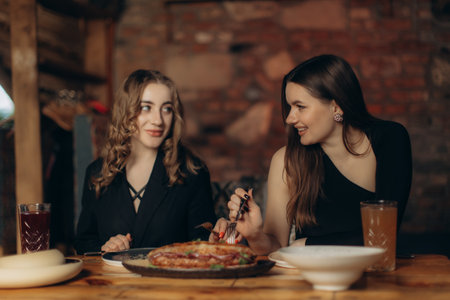 Two women share a delightful meal in a warmly decorated restaurant, emphasizing friendship and joy. The cozy ambiance enhances the experience, creating a timeless moment of connection and satisfaction.の写真素材