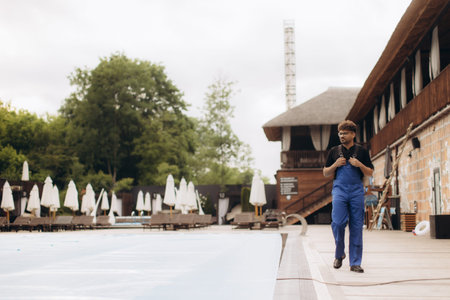 Pool maintenance worker walking near the empty pool of a resort during daytime, checking the area