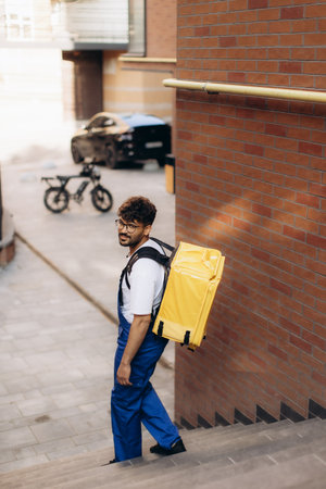 Delivery man climbing stairs with an insulated backpack, navigating the urban landscape while delivering food from local restaurantsの写真素材