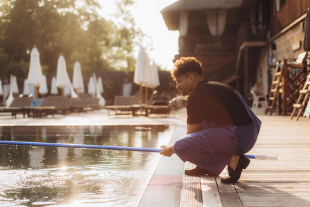 Professional pool cleaner using a telescopic pole to clean a swimming pool at a luxury resort at sunriseの写真素材