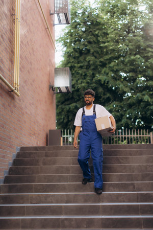 Courier walking up the stairs, carrying a cardboard box while delivering a package, showcasing the hustle of modern delivery serviceの写真素材