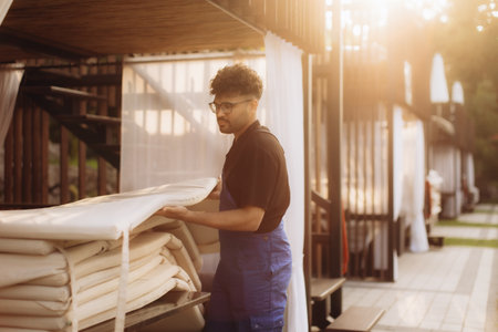 Diligent hotel worker preparing comfortable lounge area by arranging cushions on outdoor furniture, ensuring a relaxing guest experienceの写真素材