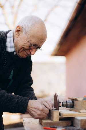 An elderly craftsman works attentively in his outdoor woodworking space, sharpening tools with precision. The afternoon sunlight enhances the warm, peaceful atmosphere of creative handiwork and dedication.の写真素材