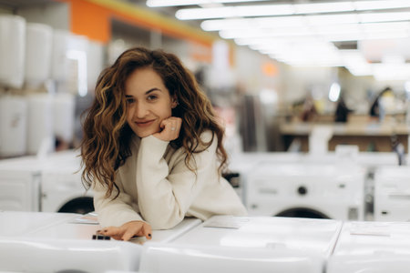 Smiling young woman in an electronics store, reviewing washing machines while enjoying her shopping.の写真素材