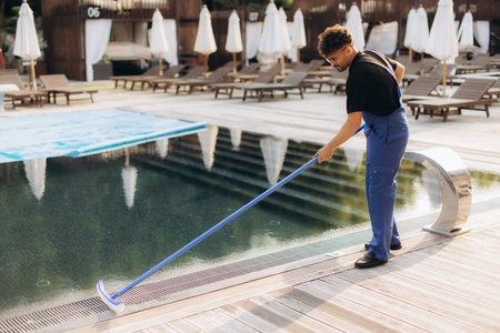 Pool cleaner is brushing the bottom of a swimming pool during his daily job in a tourist resortの写真素材