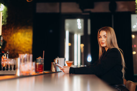 A stylish young woman sitting at a bar counter, enjoying drinks in a modern and cozy environment, embodying vibrant nightlife and social atmosphere.の写真素材
