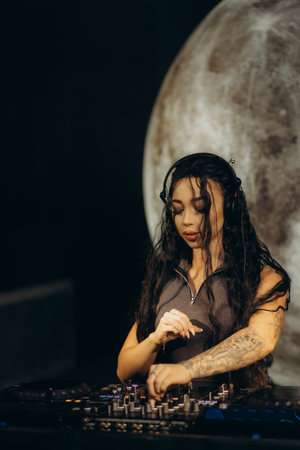 A female DJ operating a professional mixer in a nightclub, focusing on her performance, with a creative moon-like background. The scene sets a dynamic yet artistic atmosphere perfect for nightlife lovers.の写真素材