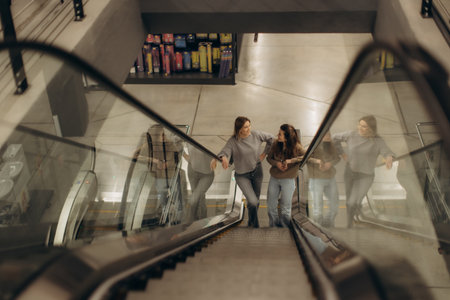 Two women engage in a friendly conversation on an escalator, surrounded by a bright indoor setting in a contemporary shopping center.の写真素材