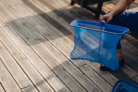 Pool cleaner holding a landing net, preparing to remove debris from the water, ensuring hygiene and maintenance in the sunny backyard poolの写真素材