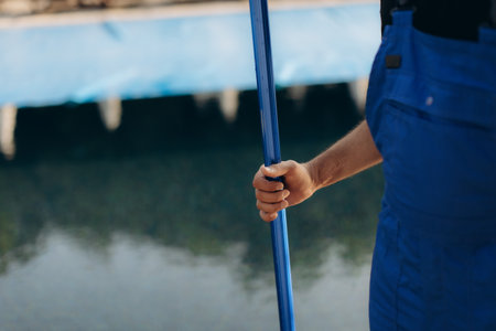 Pool cleaner holding a telescopic pole, preparing to clean a swimming pool covered with a blue tarpの写真素材