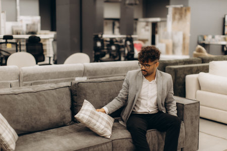 A man in a contemporary furniture store evaluates a sofa, considering design and comfort. Ideal for lifestyle, shopping, and interior design themes.の写真素材