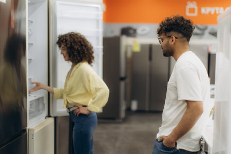 A couple examines modern refrigerators in a store display, deciding on the perfect choice. The vibrant setting emphasizes their interest in advanced home appliances.の写真素材