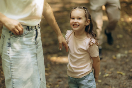 A cheerful young girl enjoying a sunny day outdoors accompanied by her family members. The setting includes a park with green surroundings, creating a joyful and familial atmosphere.の写真素材