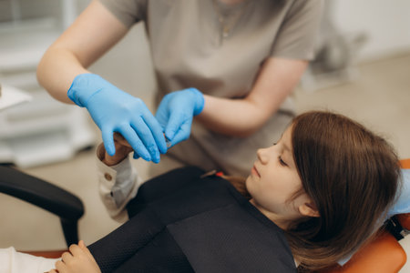 Dentist wearing blue gloves showing a tooth model to a young girl lying on a dental chair during a consultation in a dental clinicの写真素材