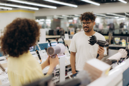 A man and a woman are discussing hairdryers, examining models displayed in an electronics store....