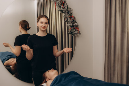 A young female spa therapist is seen assisting a patient during a session in a cozy, decorated wellness setting, embodying relaxation, care, and the festive ambiance of the season.の写真素材