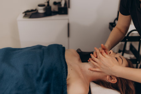 A professional massage therapist performing a facial massage on a tranquil woman. The setting emphasizes relaxation and wellness in a serene spa environment promoting healthy beauty routines.の写真素材